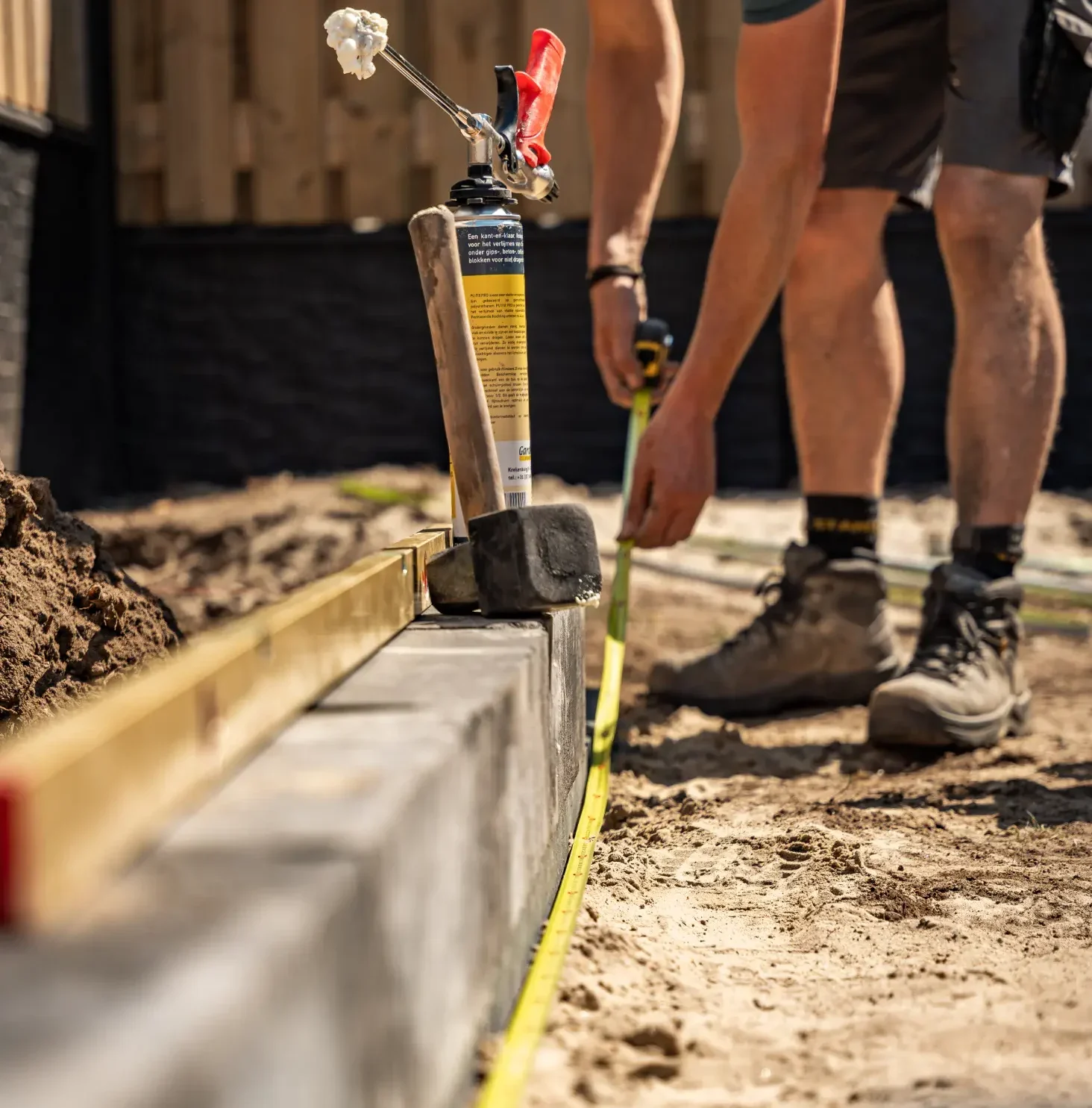 Tuinaanleg van een moderne tuin in Malden. Waar een stapelblokmuur wordt gelegd met een waterpas en meetlint voor de juiste afmeting. Tuinontwerp, tuinaanleg en tuinonderhoud door Uw Tuin, hoveniersbedrijf uit Malden